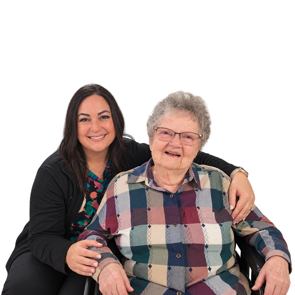 Young woman hugs an elderly woman in a plaid shirt; both smile at the camera.