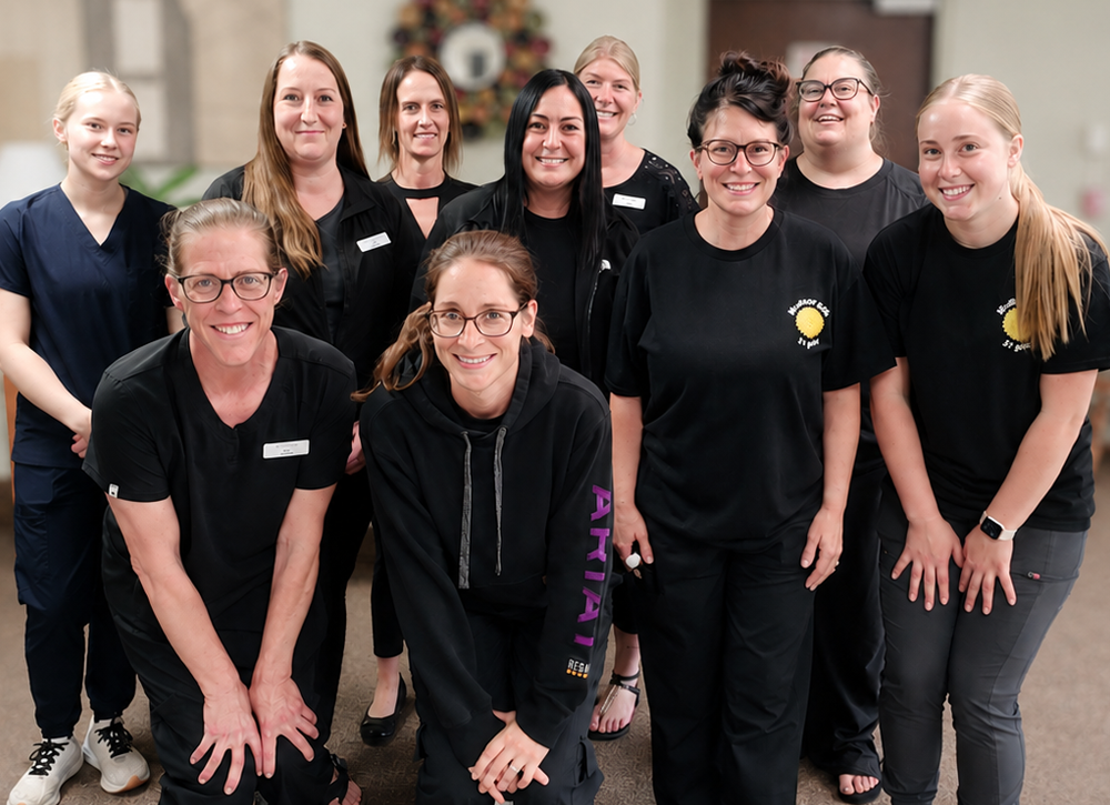 Group of ten women in black uniforms posing together indoors, smiling at the camera.